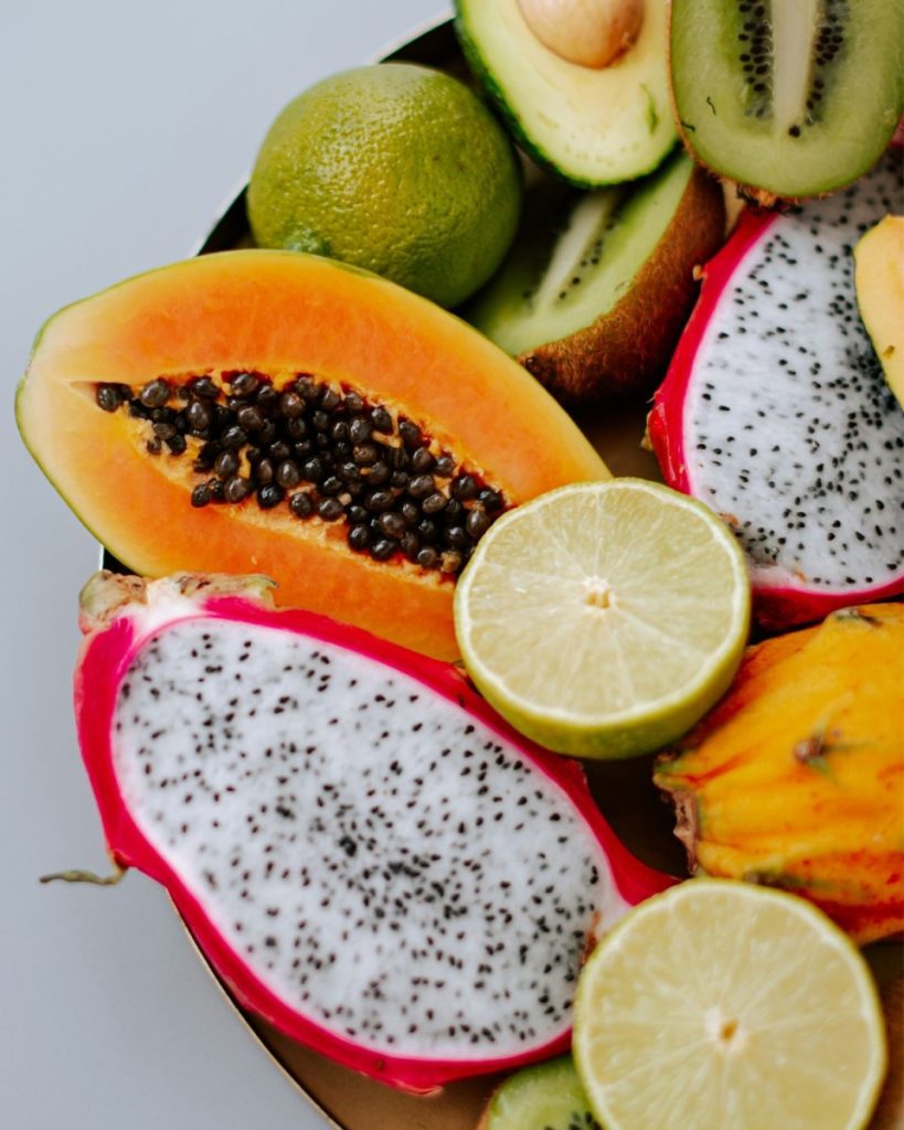 Halved papaya, dragon fruit, lime, and kiwi in vivid color. Papaya's natural enzymes speed skin cell turnover while citrus delivers vitamin C alongside the bioflavonoids your skin actually needs to use it to get that raw food glow.