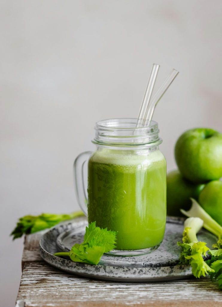 Celery juice on a wooden table with some celery stalks and green apples.