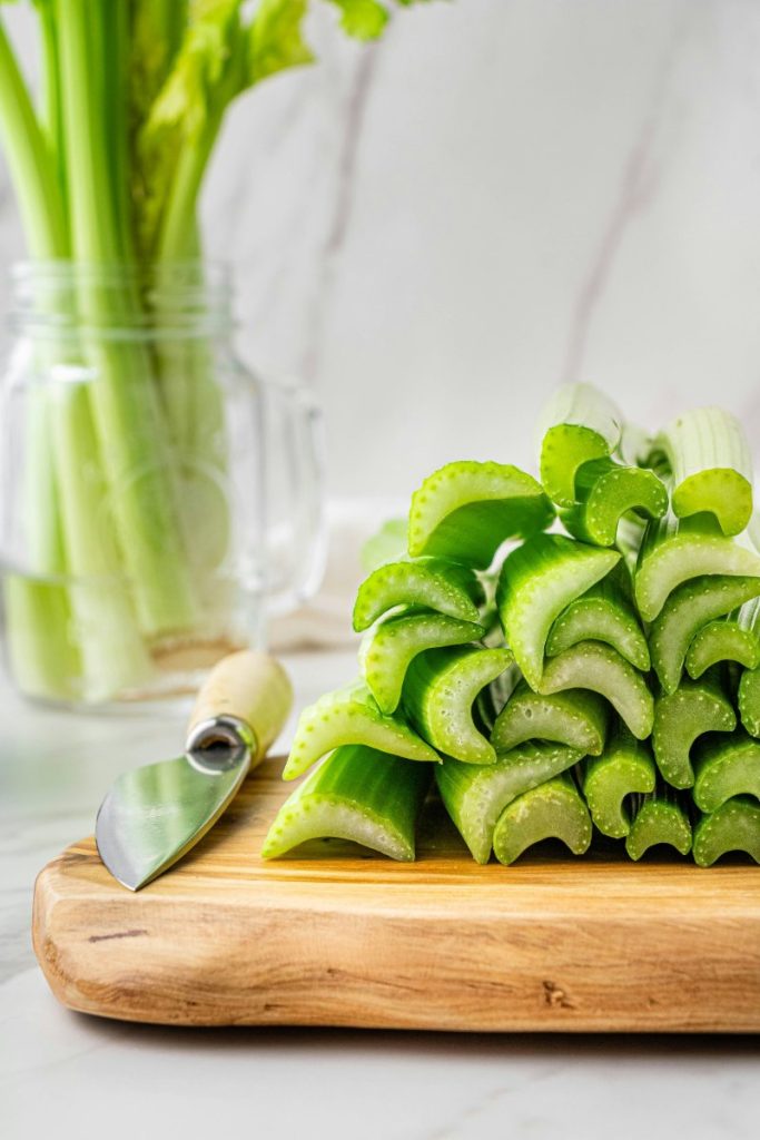 Celery stalks on a wooden chop board with a knife ready to be juiced for those incredible celery health benefits.