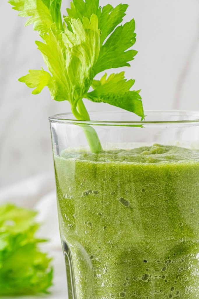 A celery smoothie with a celery leaf inside the glass as decoration.
