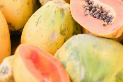 Fresh ripe papayas piled together, some halved to reveal vibrant orange flesh and black seeds — papaya benefits for digestion begin with choosing fruit at its ripest