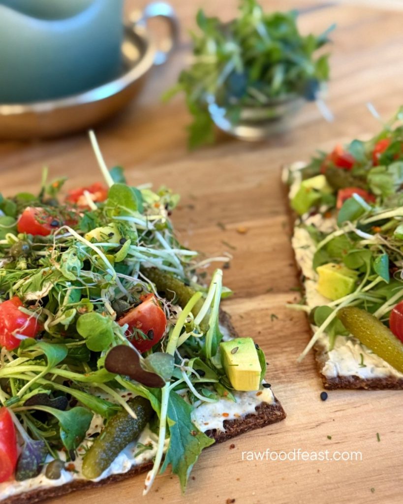Close-up of almond carrot pulp flatbread with sprouts, avocado cubes, cherry tomatoes, cornichons, and fresh cilantro — raw vegan zero-waste recipe