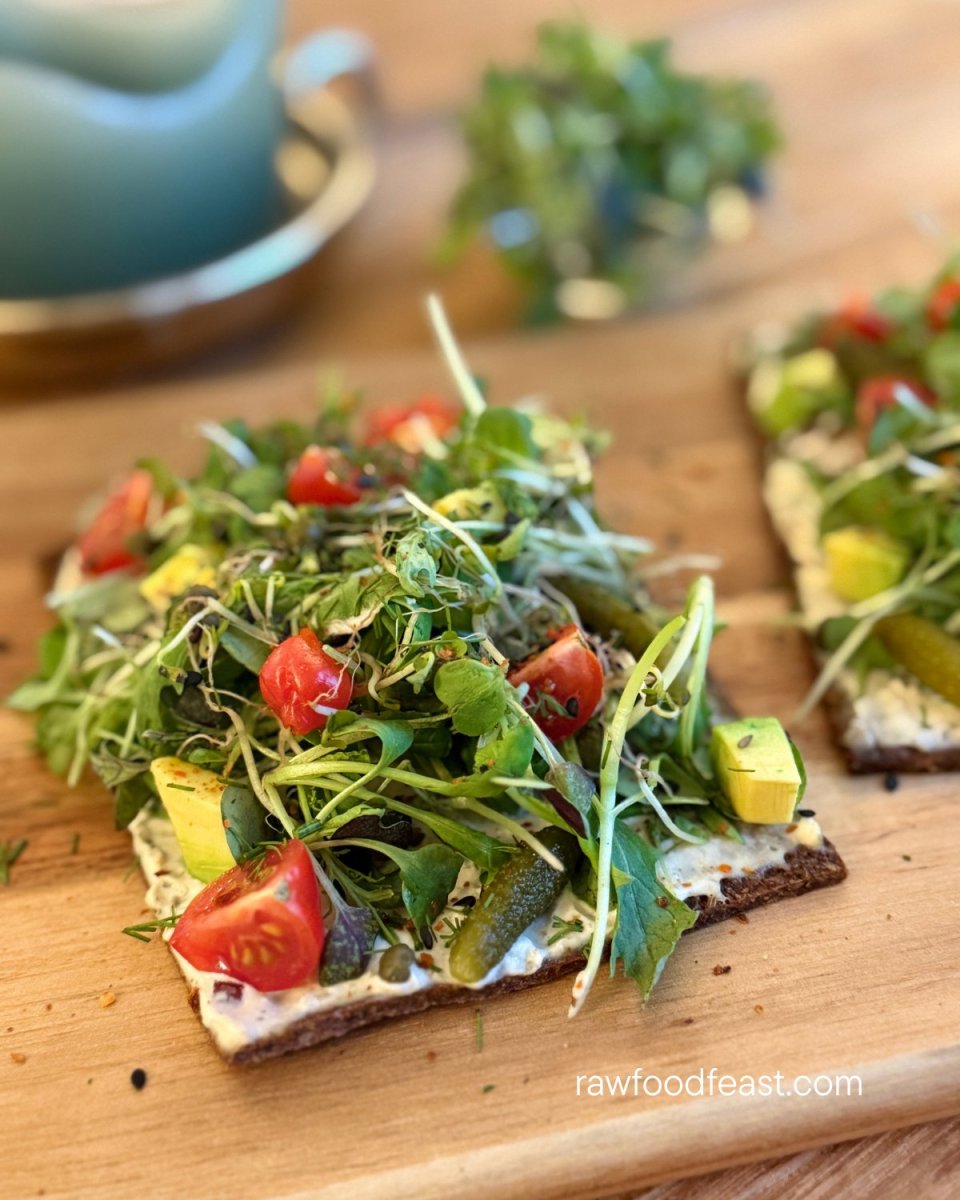 Sliced almond carrot pulp flatbread loaded with sprouts, avocado, cherry tomatoes, and cornichons — fiber-rich dehydrated raw vegan flatbread