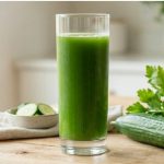 Tall glass of green juice with celery and cucumber on a light wood surface — does juicing help with microplastics through daily liver and lymph support