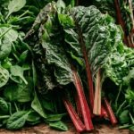 Fresh kale, swiss chard, and leafy greens on a light wood surface — the foods that remove microplastics starting in the gut