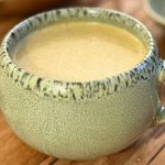 Golden milk recipe in a ceramic mug with fresh turmeric root and cashews on a wooden surface