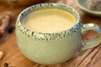 Golden milk recipe in a ceramic mug with fresh turmeric root and cashews on a wooden surface