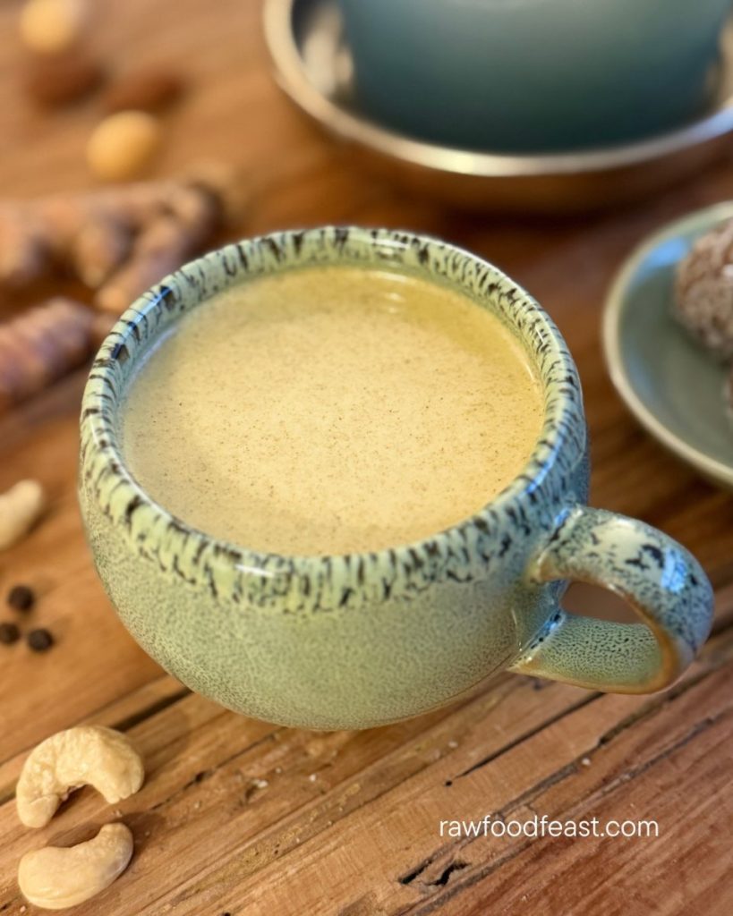 Homemade golden milk recipe in a handmade ceramic mug with cashews and golden glow balls on a wooden surface