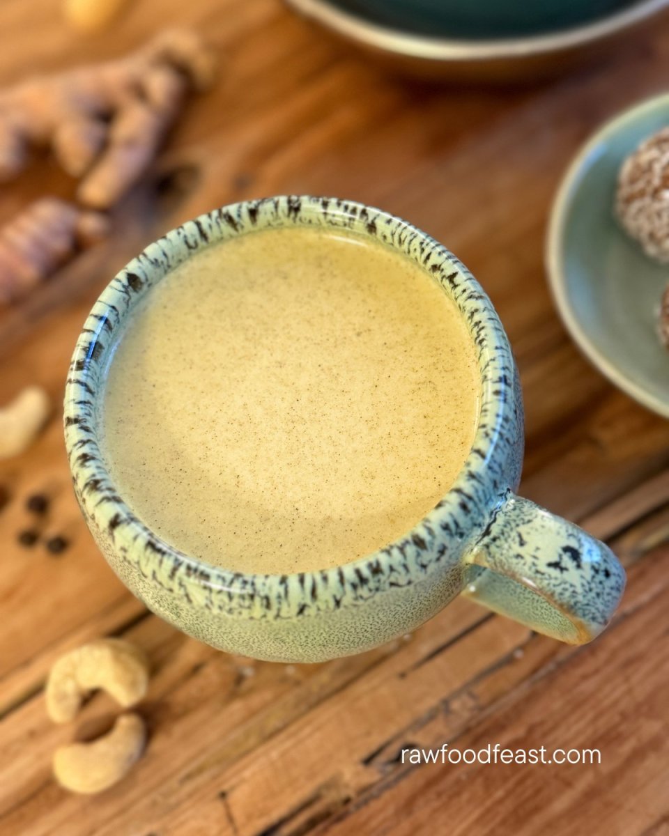 Golden milk recipe viewed from above in a ceramic mug surrounded by turmeric root, cashews, and golden glow balls