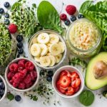 Gut-brain connection — leafy greens, sprouts, blueberries, raspberries, banana, avocado, sauerkraut, and green juice on a clean white surface