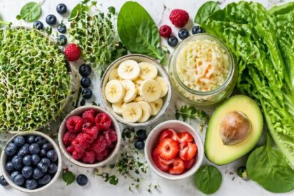 Gut-brain connection — leafy greens, sprouts, blueberries, raspberries, banana, avocado, sauerkraut, and green juice on a clean white surface