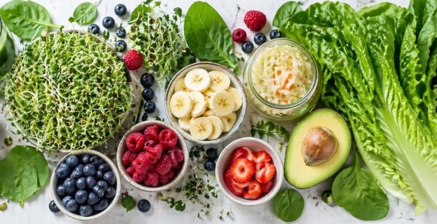 Gut-brain connection — leafy greens, sprouts, blueberries, raspberries, banana, avocado, sauerkraut, and green juice on a clean white surface