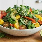 Iron on a raw food diet — vibrant raw food salad bowl with spinach, strawberries, avocado, mango, orange and microgreens on warm natural wood