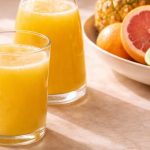Pineapple juice benefits — three glasses of fresh cold-pressed pineapple juice on a warm natural surface with citrus fruit