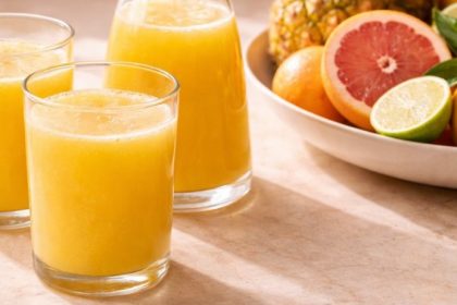 Pineapple juice benefits — three glasses of fresh cold-pressed pineapple juice on a warm natural surface with citrus fruit