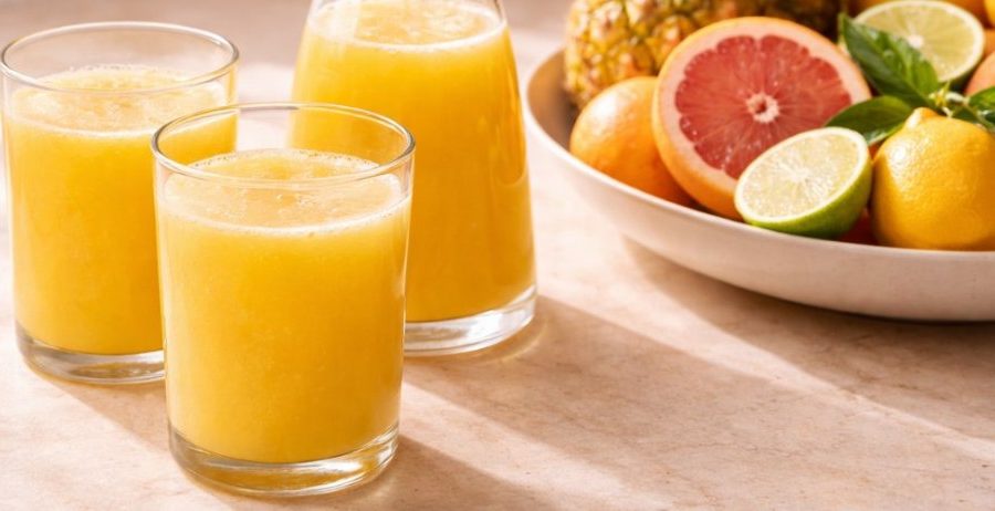 Pineapple juice benefits — three glasses of fresh cold-pressed pineapple juice on a warm natural surface with citrus fruit