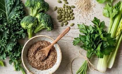 Raw food perimenopause spread — kale, broccoli, celery, seeds, berries, and lemon on a light wood surface