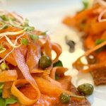 Close-up of raw sundried tomato crackers piled with marinated carrot ribbons, capers, and sprouts — oil-free, gluten-free, made in the dehydrator
