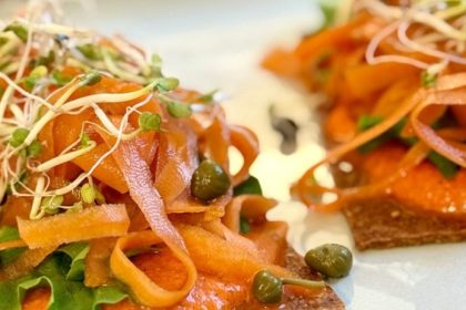 Close-up of raw sundried tomato crackers piled with marinated carrot ribbons, capers, and sprouts — oil-free, gluten-free, made in the dehydrator