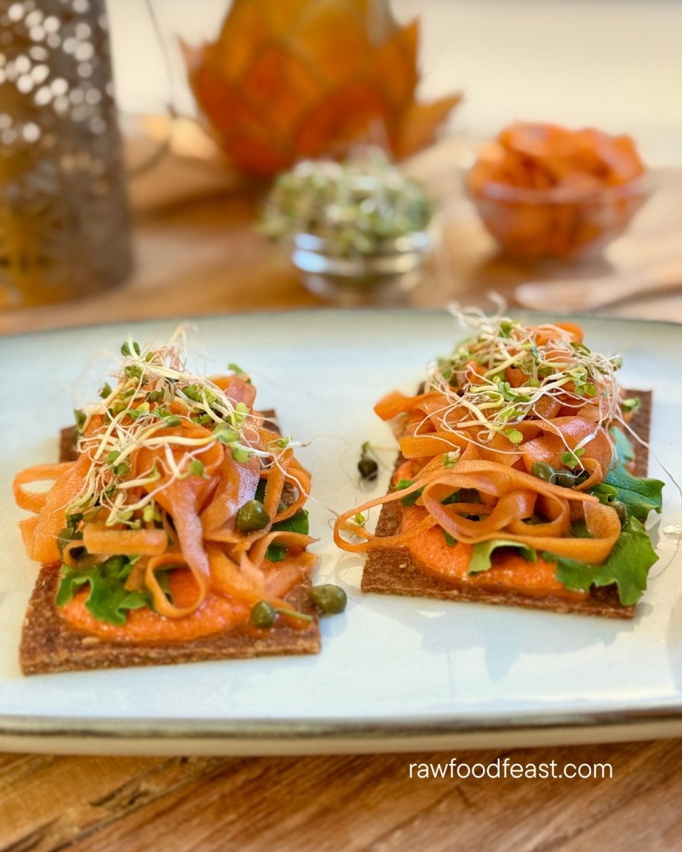 Two raw vegan sundried tomato crackers on a round plate with marinated carrot ribbons, sprouts, capers, and a side bowl of creamy bell pepper dressing — plant-packed raw vegan meal