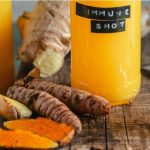 Turmeric juice benefits — golden immune shot glass with fresh turmeric, ginger, and citrus on a rustic wood surface