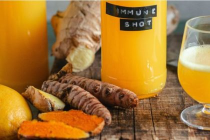 Turmeric juice benefits — golden immune shot glass with fresh turmeric, ginger, and citrus on a rustic wood surface