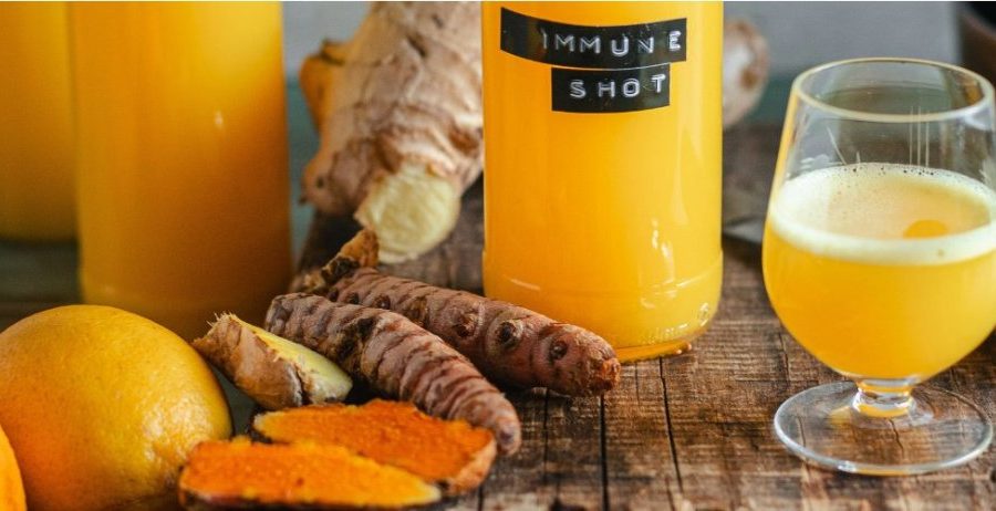 Turmeric juice benefits — golden immune shot glass with fresh turmeric, ginger, and citrus on a rustic wood surface