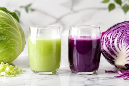 Whole green cabbage and halved red cabbage with two glasses of cabbage juice on white marble — cabbage juice for gut health