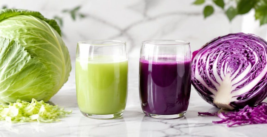 Whole green cabbage and halved red cabbage with two glasses of cabbage juice on white marble — cabbage juice for gut health