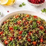 Raw cauliflower tabbouleh with pomegranate seeds, fresh herbs, cherry tomatoes, lemon, and sumac on a white marble. counter