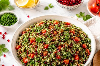 Raw cauliflower tabbouleh with pomegranate seeds, fresh herbs, cherry tomatoes, lemon, and sumac on a white marble. counter