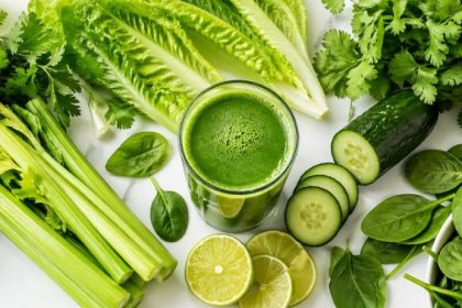 Green juice benefits — fresh cold-pressed green juice surrounded by parsley, romaine, celery, spinach, cucumber, cilantro, and lime on a clean white surface