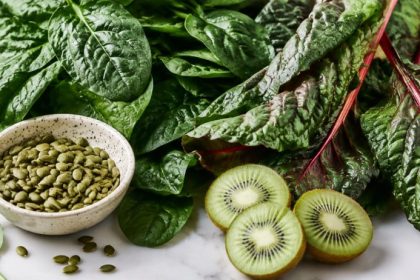 Spinach, swiss chard, pumpkin seeds, and fresh kiwi on white marble — foods for gut health and sleep.