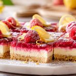 No bake lemon raspberry bars with a coconut date crust, cashew lemon filling, and fresh raspberry layer on a white plate