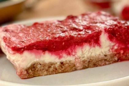 No bake lemon raspberry bars with a coconut date crust, cashew lemon filling, and fresh raspberry layer on a white plate