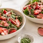 Two bowls of raw strawberry spinach salad with pink strawberry balsamic dressing and fresh basil