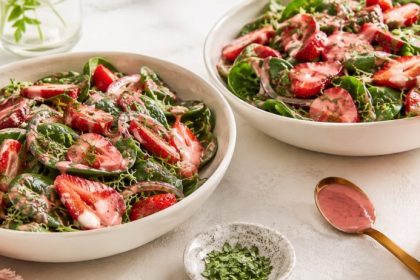 Two bowls of raw strawberry spinach salad with pink strawberry balsamic dressing and fresh basil