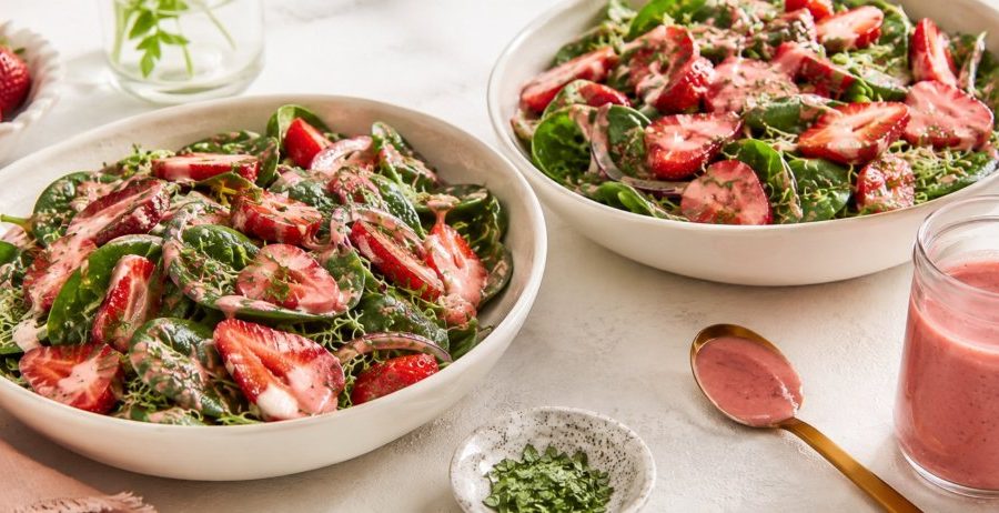 Two bowls of raw strawberry spinach salad with pink strawberry balsamic dressing and fresh basil