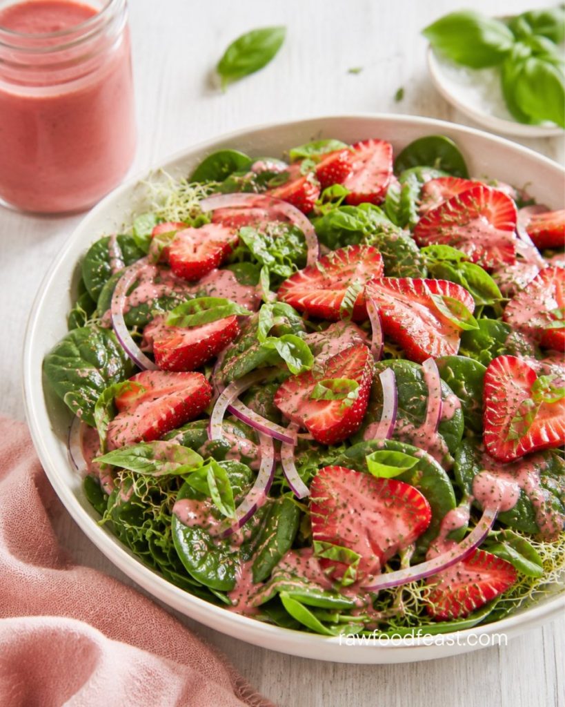 Close-up of a single raw strawberry spinach salad bowl tossed in pink strawberry balsamic dressing