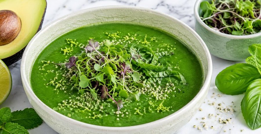 A cream crackle bowl of green gazpacho topped with microgreens, basil, and lime zest on marble — green glow gazpacho.