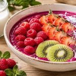 Pink pitaya smoothie bowl with raspberries, strawberries, kiwi, coconut shred, and chia seeds